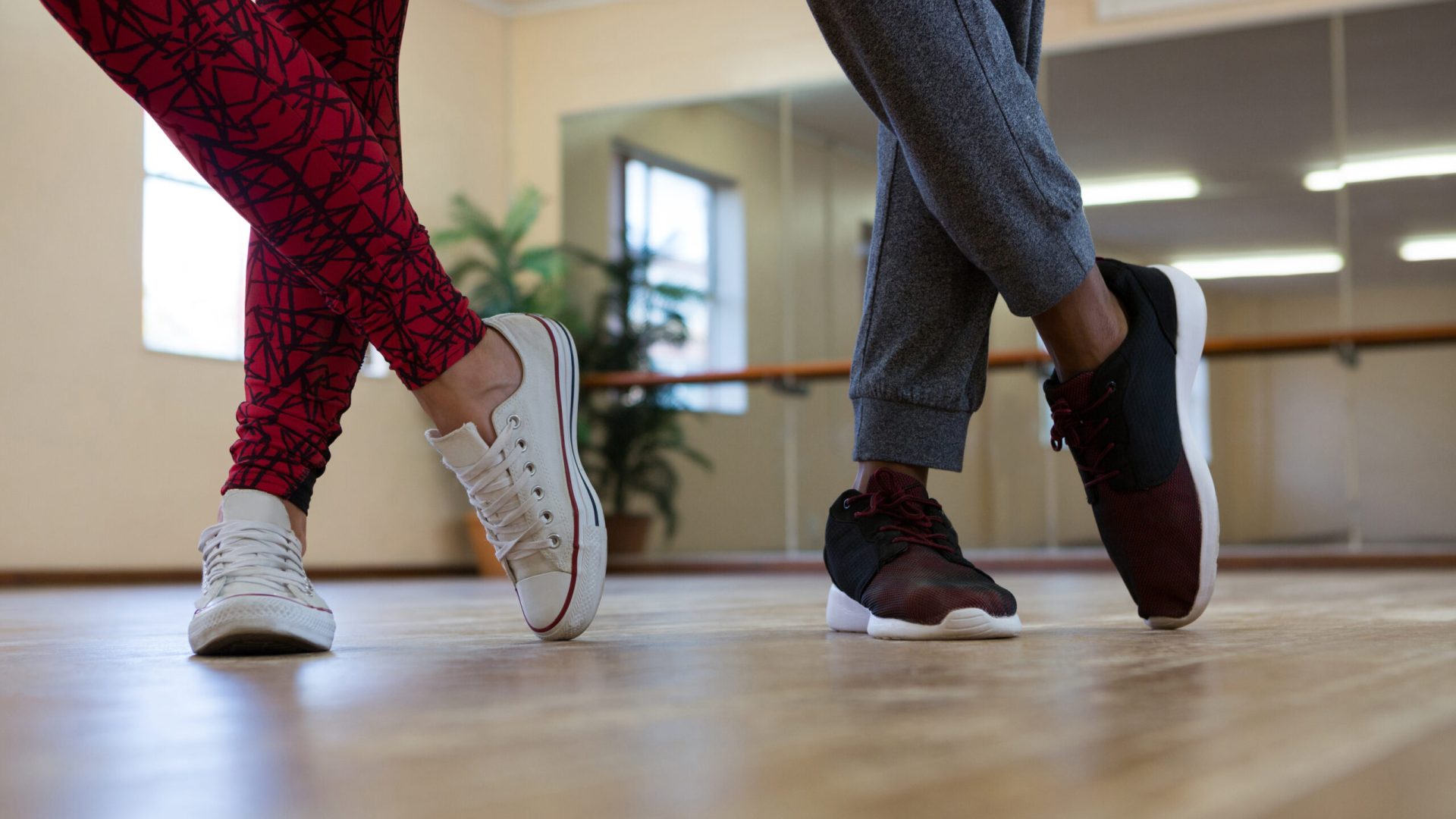Low section of friends practicing dance on wooden floor in studio